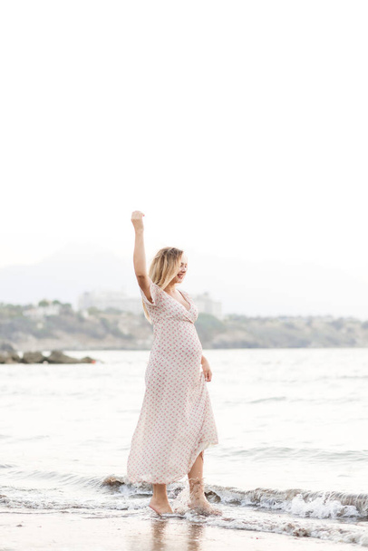 Happy young pregnant woman in a long dress walks on the sea beach.Lifestyle happienest concept - 写真・画像