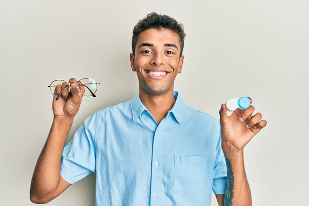 Young handsome african american man holding glasses and contact lenses smiling with a happy and cool smile on face. showing teeth.  - Foto, Bild