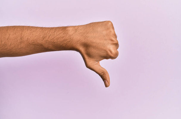 Braço e mão do jovem caucasiano sobre fundo isolado rosa fazendo polegares para baixo gesto de rejeição, desaprovação antipatia e sinal negativo  - Foto, Imagem