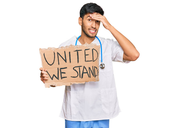 Jonge knappe man in doktersuniform verenigd staan we spandoek gestrest en gefrustreerd met hand op hoofd, verrast en boos gezicht  - Foto, afbeelding