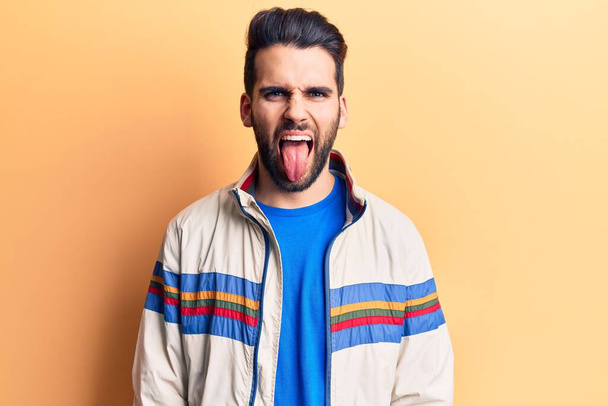 Young handsome man with beard wearing casual jacket sticking tongue out happy with funny expression. emotion concept.  - Foto, Imagen
