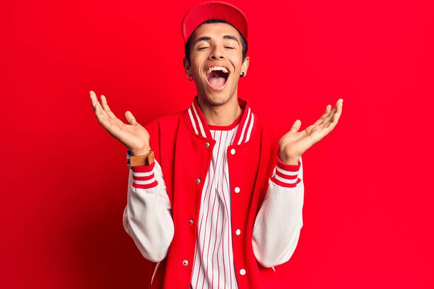 Young african amercian man wearing baseball uniform celebrating mad and crazy for success with arms raised and closed eyes screaming excited. winner concept  - Fotografie, Obrázek