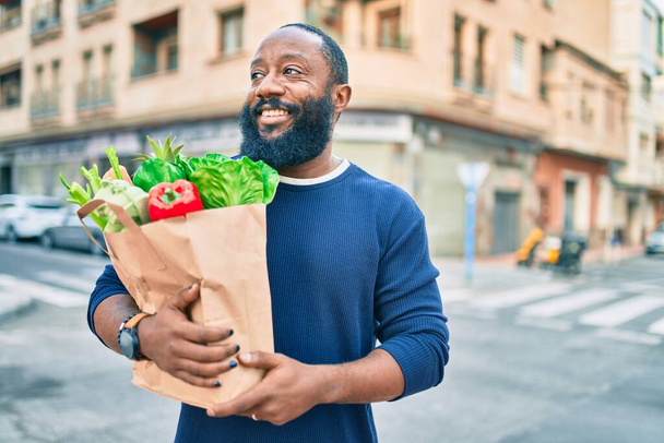 アフリカ系アメリカ人で髭を生やした男がスーパーマーケットから食料品の袋を持っている - 写真・画像