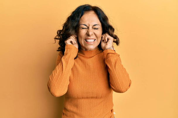 Femme hispanique du Moyen Âge portant des vêtements décontractés couvrant les oreilles avec des doigts avec une expression agacée pour le bruit de la musique forte. concept sourd.  - Photo, image