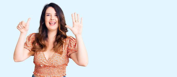 Schöne junge brünette Frau trägt lässige Kleidung und zeigt mit Fingern Nummer sechs nach oben, während sie selbstbewusst und glücklich lächelt.  - Foto, Bild