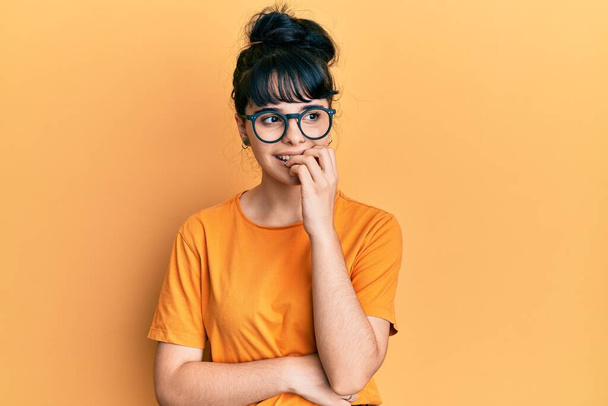Jong Latijns-Amerikaans meisje draagt casual kleren en glazen kijken gestresst en nerveus met handen op de mond bijtende nagels. angstprobleem.  - Foto, afbeelding