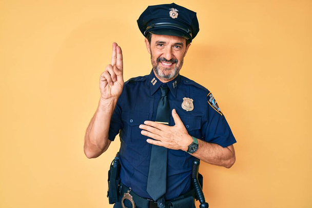 Середньовіччя іспаномовний чоловік у поліцейській формі посміхається лаятися з рукою на грудях і пальцях вгору, роблячи клятву обіцянки лояльності
  - Фото, зображення