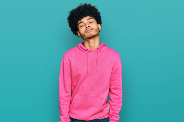Молодий афроамериканець з волоссям афроамериканського кольору, одягнений у звичайний рожевий светр, розслаблений серйозним виразом обличчя. Звичайний і природний погляд на камеру..  - Фото, зображення