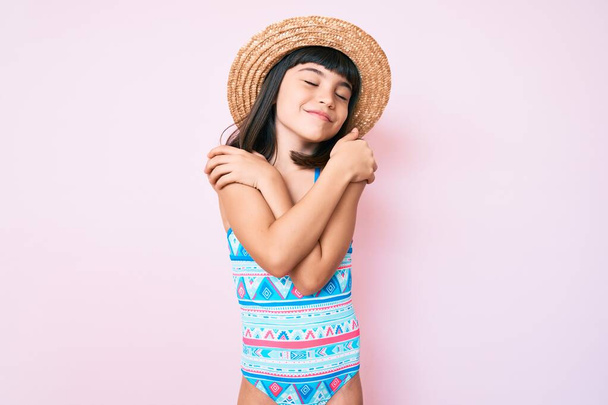 Fiatal lány, aki fürdőruhában és nyári kalapban ölelkezik, boldog és pozitív, mosolygós magabiztos. önszeretet és öngondoskodás  - Fotó, kép