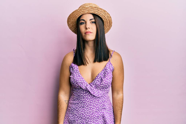 Young brunette woman wearing summer dress and hat relaxed with serious expression on face. simple and natural looking at the camera.  - Photo, Image