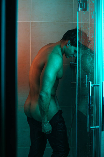 Un stripper en la ducha. Un guapo desnudo quitándose los pantalones en la ducha. Cuerpo masculino húmedo en el baño. - Foto, imagen