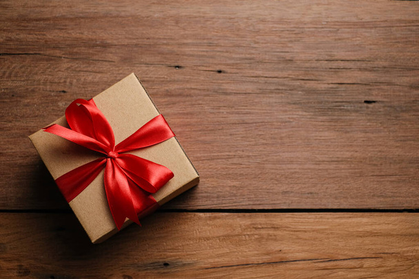 Selective focus of gift box with red ribbon and love shaped paper over rustic wooden table, top view flat lay. - Photo, Image