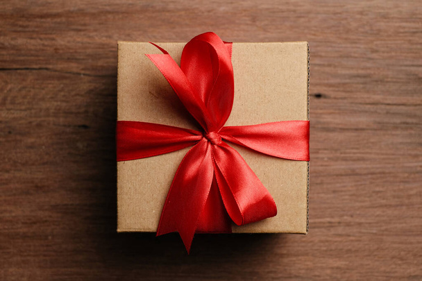 Επιλεκτική εστίαση της συσκευασίας δώρου με κόκκινη κορδέλα και χαρτί σε σχήμα αγάπης πάνω από ρουστίκ ξύλινο τραπέζι, πάνω όψη επίπεδη lay. - Φωτογραφία, εικόνα