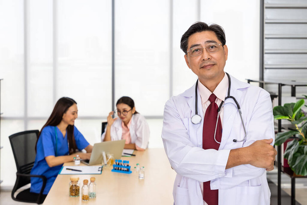 Ritratto di un anziano medico asiatico con le braccia incrociate davanti alla riunione della squadra - Foto, immagini