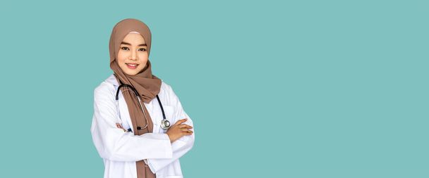Magabiztos muszlim női orvosnő áll és keresztezi a karját sztetoszkóppal világoszöld háttérrel; a kamerába néz - Fotó, kép