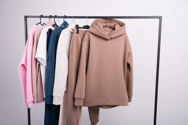 Women's minimal fashion pastel clothes. Stylish female t-shirts, hoodie, pants on hanger on white background. Spring cleaning home wardrobe. High quality photo - Fotografie, Obrázek