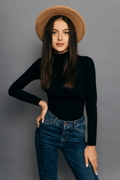 Beautiful girl in black body suit, jean and straw hat, isolated on grey background - Fotografie, Obrázek