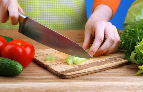 Female hands cutting celery on wooden board, close-up, on blue background - Fotografie, Obrázek