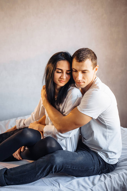 Handsome man with a pumped-up body imperiously hugs his girlfriend. Ready to have sex in a snow-white bed at home. They embrace sensibly during foreplay. Hold each other's hands. - Фото, изображение