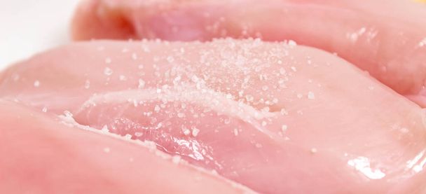 Raw chicken fillet close-up, on which salt is sprinkled on top. selective shot. The horizontal frame. - Φωτογραφία, εικόνα