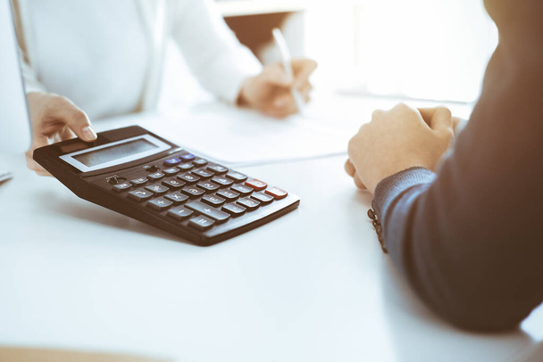 Accountant checking financial statement or counting by calculator income for tax form, hands close-up. Business woman sitting and working with colleague at the desk in office. Audit concept - Foto, imagen