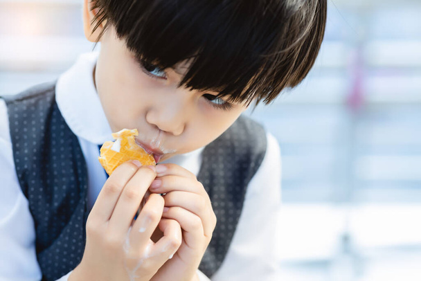 Niedliches kleines Kind isst gerne Süßigkeiten oder Eis. Schöner kleiner Junge isst so gerne Eis in der Stadt. Liebenswertes Kind isst gerne leckere Süßigkeiten. Er fühlt sich glücklich, wenn er Lieblingsdessert isst - Foto, Bild