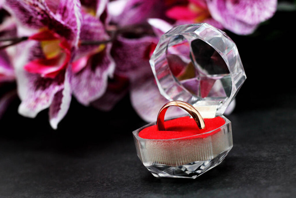 золотое обручальное кольцо в стеклянной коробке на фоне орхидеи, любовь и счастье - Фото, изображение