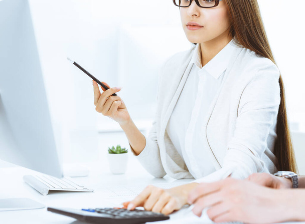 Young business woman and man sitting and working with computer and calculator in office. Bookkeeper checking balance or making finance report. Tax and audit concepts - Φωτογραφία, εικόνα