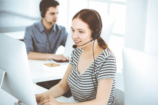 Mujer joven vestida casual usando auriculares y computadora mientras habla con los clientes en línea. Grupo de operadores en el trabajo. Call center, concepto de negocio - Foto, Imagen