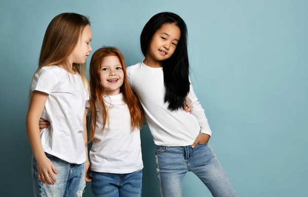 Mixed race international happy girls friends in jeans and white t-shirts standing and hugging together smiling laughing  - 写真・画像