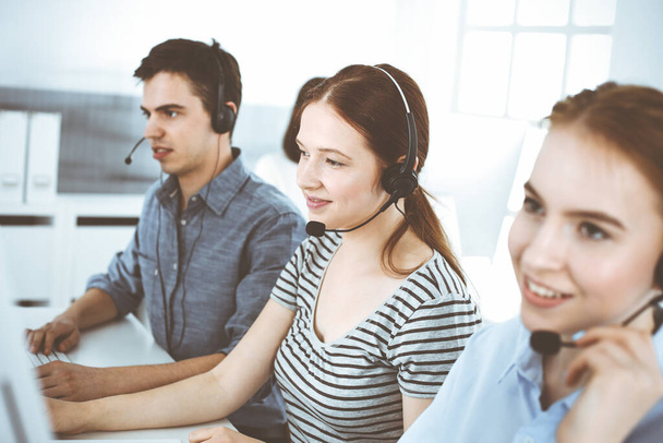 Mujer joven vestida casual usando auriculares y computadora mientras habla con los clientes en línea. Grupo de operadores en el trabajo. Call center, concepto de negocio - Foto, imagen