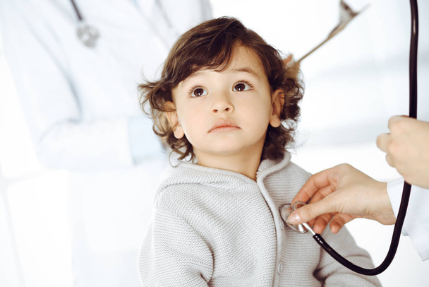 Woman-doctor examining a child patient by stethoscope. Cute arab toddler at physician appointment. Medicine concept - Photo, image