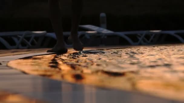 Barefoot loopt bij het zwembad bij zonsondergang. Golven in het zwembad. De golven van het zwembad raakte zijn voeten - 4K - Video
