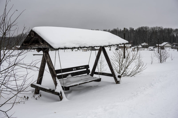 un banco con protección solar se encuentra en un campo cubierto de nieve - Foto, Imagen