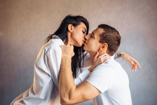 Ελκυστικό, νεαρό ζευγάρι εραστών που κάνουν σεξ στο σπίτι στο κρεβάτι σε φωτεινό δωμάτιο. Κορίτσι που φιλάει το αγόρι της περίεργα, τραβώντας απαλά το κάτω χείλος του. Γιορτάζοντας την Ημέρα του Αγίου Βαλεντίνου - 14 Φεβρουαρίου. - Φωτογραφία, εικόνα
