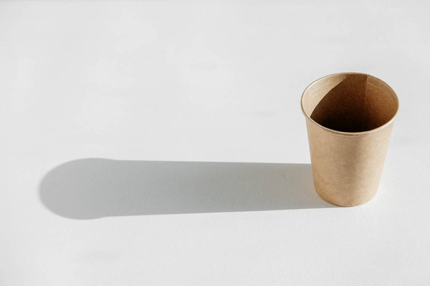 Disposable paper cup with shadow from light on a white background. Copy, empty space for text. - Photo, Image