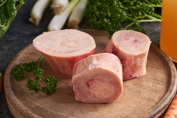 Ingrediënten voor de bereiding van bouillon of soep van rundvlees - verse beenderen en groenten op de achtergrond - Foto, afbeelding