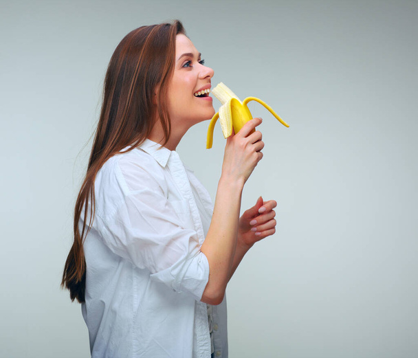 Woman in dressed casual eating banana and looking away. isolated female portrait. - Foto, immagini