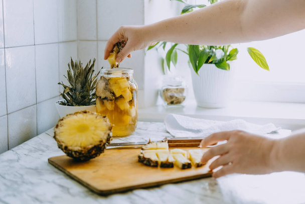 Sfermentowana ananasowa kombucha pije tepache. Proces gotowania domowego probiotycznego napoju ananasowego. Słoik na napoje i pokrojony ananas na domowej kuchni - Zdjęcie, obraz