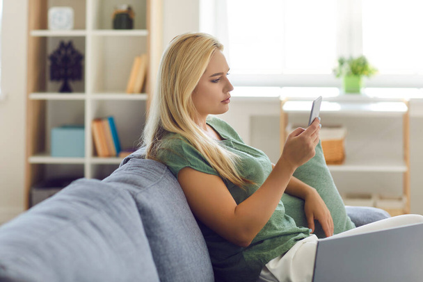 Жінка сидить на дивані, використовуючи мобільний телефон, щоб спілкуватися в соціальних мережах або купувати речі в інтернет-магазині
 - Фото, зображення