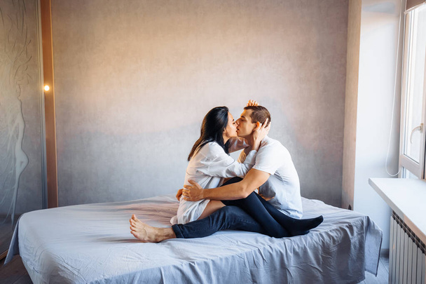 魅力的で、若い恋人のカップルは明るい部屋のベッドで自宅でセックスをしています。女の子は奇妙な彼女のボーイフレンドにキスをし、優しく彼の下唇を引き戻す。バレンタインデーを祝う- 2月14日. - 写真・画像