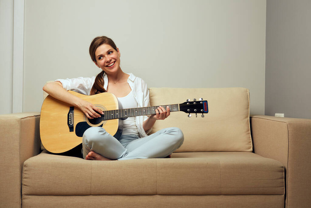 Young woman playing on guitar sitting on sofa. - Fotoğraf, Görsel