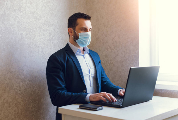 Людина в медичній масці і куртці працює на ноутбуці
. - Фото, зображення