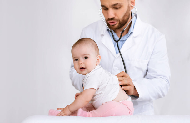 Arzt untersucht Baby, das vor weißem Hintergrund auf ihre Lungen hört - Foto, Bild