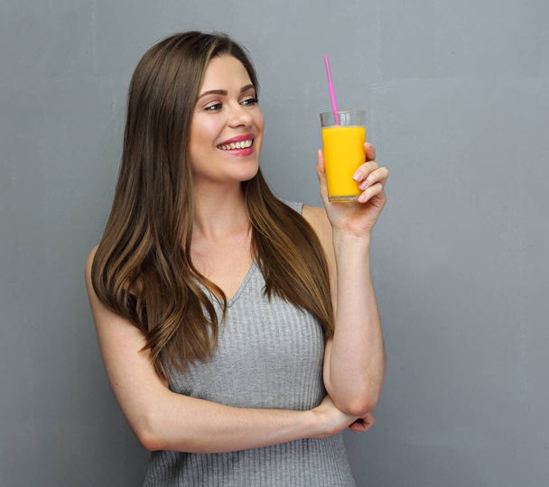 Smiling woman holding orange juice glass. Gray wall background. - Фото, зображення