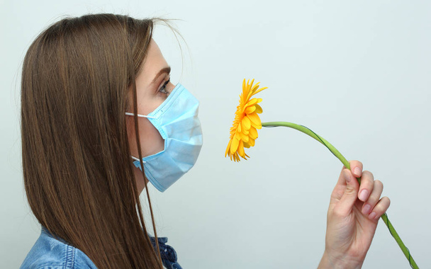 Woman wearing medical mask sniffs flower. Allergies reaction concept portrait. - Fotó, kép
