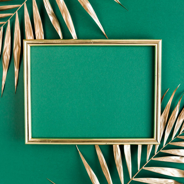 Gold tropical palm leaves and photo frame on green background. Flat lay, top view minimal concept. - Fotoğraf, Görsel