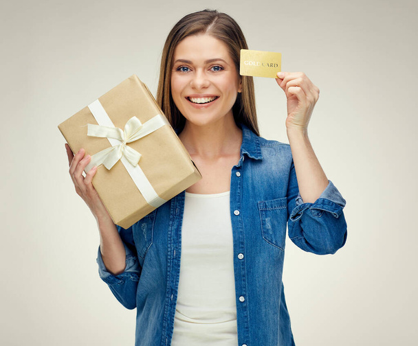 Usmívající se žena drží kreditku blízko oka. Dívka s dárkovou krabicí izolované studio portrét. - Fotografie, Obrázek