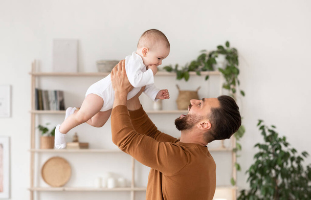 Vater spielt zu Hause mit Baby, das Kind über dem Kopf hält - Foto, Bild