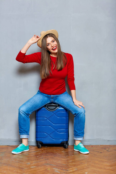Traveler woman sitting at suitcase. Gray wall studio background. - 写真・画像
